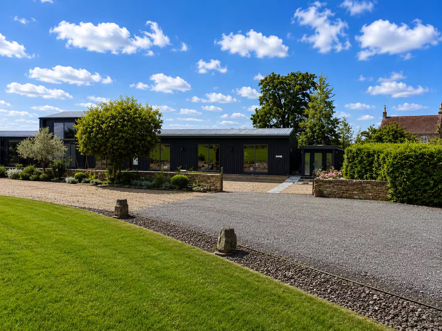 Faraway Barn — a black timber barn conversion with a gravel drive under a wide blue sky